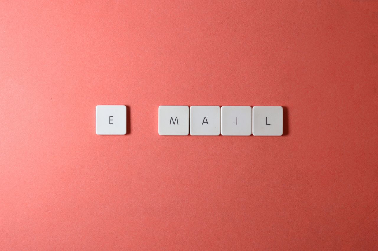 services-02 Flat lay of keyboard letter tiles spelling email on coral backdrop.